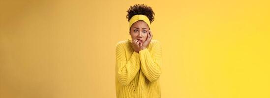 Afraid concerned nervous young african american female employee worried anxious be fired clench teeth stooping touch face insecure bit fingers standing scared terrified, yellow background photo