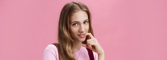 Cute feminine girl learning how make glances and seduce boyfriend with flirty gaze biting finger sensually posing against pink background, flirting making senducing look wearing make-up on date photo