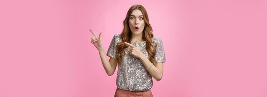 Amused attractive european woman see awesome promo pointing upper right corner sideways thrilled say wow folding lips astonished excited widen eyes impressed surprised, standing pink background photo