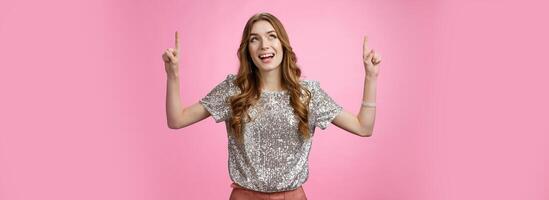 Charming excited good-looking glamour young girl look up thrilled joyful pointing index finger top upwards smiling amazed enjoyment perfect weather, standing happily pink background photo