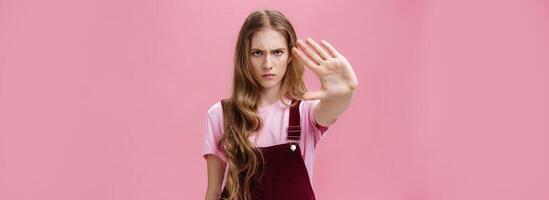 Woman protest against testing products on animals. Serious-looking confident young girl with long wavy hair frowning looking sctrict at camera pulling palm towards camera in prohibition and no gesture photo