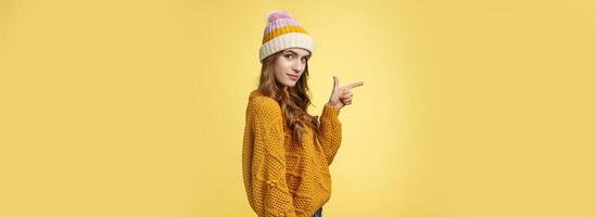 Profile shot confident flirty fashionable young 20s girl turning camera smiling pointing left inviting go together showing curious promotion cool place hang out, standing yellow background relaxed photo
