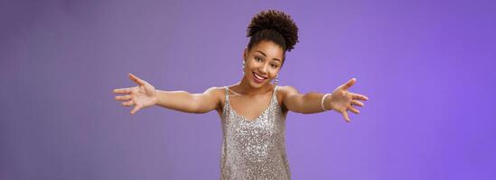 Lovely touched african-american female in evening slver dress extend arms hug give cuddle tilt head smiling friendly wanna ebrace friend gladly standing blue background heartwarming welcome photo