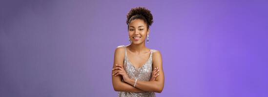Stylish elegant tender african woman party in stylish silver glittering evening dress hold hands crossed chest self-assured friendly casual pose smiling broadly talking, conversation during party photo