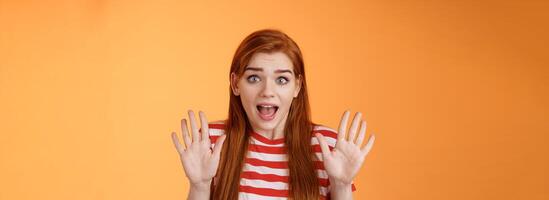 Shocked inssecure worried redhead woman plead not guilty, trying calm down angry customer, raise hands surrender innocent, open mouth, stare concerned camera, defend herself, explain situation photo