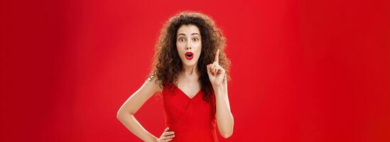 Got excellent idea listen. Portrait of creative friendly and smart attractive caucasian woman in elegant red dress with evening make-up gasping adding suggestion raising index finger in eureka gesture photo