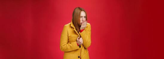 Girl getting cold, coughing and buttoning yelling light coat as freezing on chilly, windy weather looking displeased and ill at camera, feeling unwell catching flu over red background photo