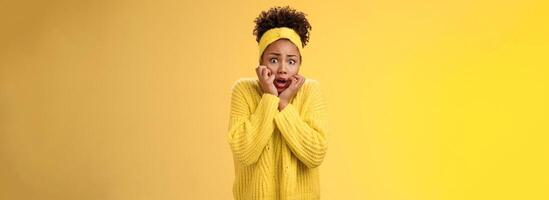 Scared stupefied trembling insecure timid african american woman afraid widen eyes gasping touching face terrified look horror eyes terrified cannot move shaking fear, standing yellow background photo