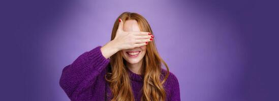 Happiness, emotions and anticipation concept. Charming dreamy ginger girlfriend with cute nails covering eyes with raised palm and smiling broadly waiting for surprise or miracle, playing peekaboo photo