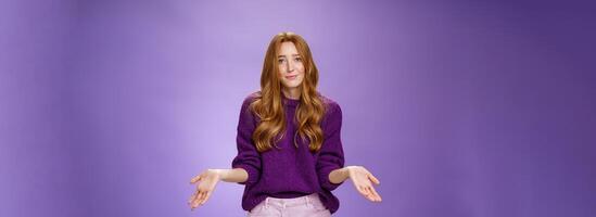 Who cares chill I not know. Portrait of clueless and unbothered cute redhead female in purple sweater smirking in sorry and shrugging with hands sideways being questioned and puzzled to answer photo