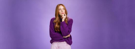 Thoughtful and focused smart, creative attractive woman with red hair and freckles squinting, looking at upper left corner while thinking having idea or plan holding hand on chin as making up choice photo