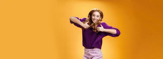 Optimistic and joyful bright ginger girl jumping happily and cheerful having fun showing thumbs up in like and approval giving positive feedback of super cool idea or concept over orange wall photo