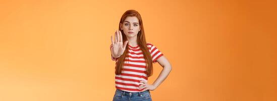 Serious-looking confident brave redhead girl oppose haters, fighting for freedom, prohibit illegal actions, extend hand stop enough, never or forbidden gesture, look determined camera photo