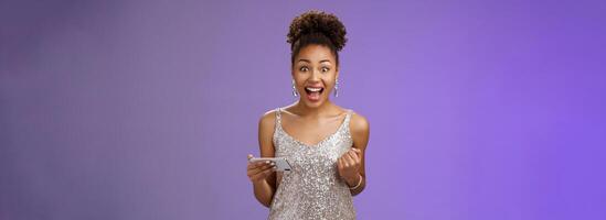 Excited charming young african-american woman lucky winning game playing smartphone standing pleased yelling happily clench fist triumphing joyfully celebrating great news received message photo