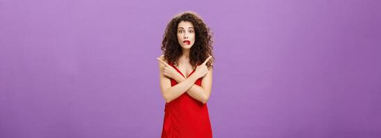Enthusiastic unsure emotive elegant woman in stylish evening red dress biting lip looking excited pointing in different directions left and right being uncertain and doubtful in making decision photo