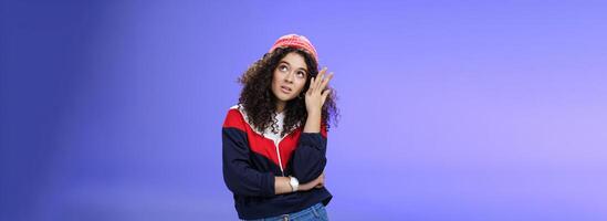 Waist-up shot of bored and annoyed assertive arrogant cool girl in streetstyle outfit rolling eyes up making facepalm and grimacing from irritation and disappointment, posing against blue background photo