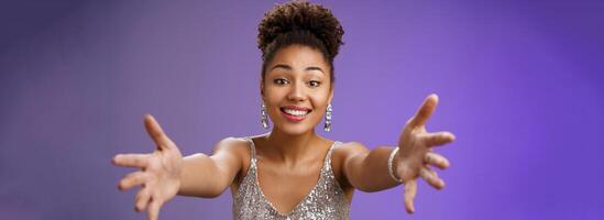 Close-up charming touched tender wealthy african-american woman in silver fashionable dress extend arms towards camera give warm welcome hug smiling delighted wanna cuddle hold in hands photo