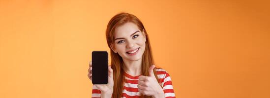 Best smartphone app guarantee. Assertive lovely friendly-looking redhead woman recommend cellphone application, introduce online store website, like give thumb-up approval, stand orange background photo