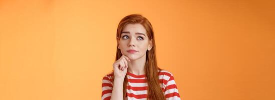 Close-up uneasy cute redhead female student facing tough troublesome decision, thinking intense, look upper left corner thoughtful touch chin, pondering between choices, frown focused photo