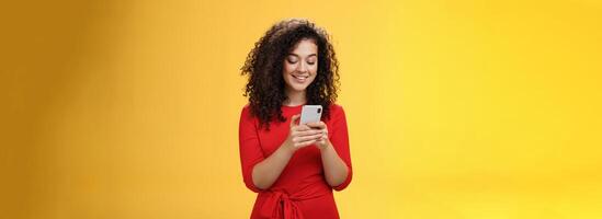 Gil sending message spread news across social network having party inviting friends via smartphone holding mobile phone in hands smiling broadly at device screen as posing over yellow background photo