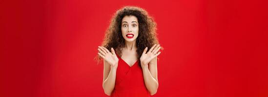 Woman feeling nervous and concerned messing up important papers clenching teeth and popping eyes being worried and troubled waving raised palms in clueless and perplexed gesture over red background photo