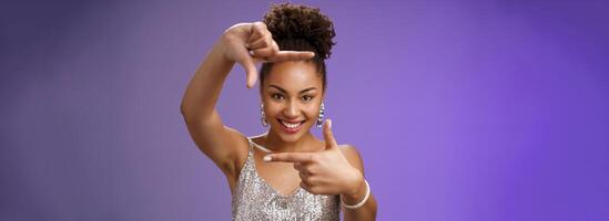 Elegant attractive happy creative african american girl in silver shiny dress make finger frames smiling through it search inspiration looking confident found perfect angle design idea, spot goal photo