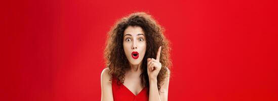 Woman remembered important information feeling excited adding suggestion with raised index finger in eureka gesture, folding lips in raising eyebrows being thrilled finally understanding photo