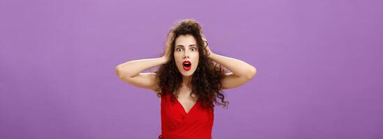 You do not say. Portrait of shocked and impressed speechless woman with curly haircut in luxurious evening dress opening mouth from amazement and shock holding hands on head stunned over puple wall photo