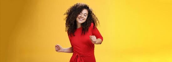 Carefree woman dancing on dance floor with close eyes and smile enjoying life feeling happy and joyful close eyes and making tender expression as moving to rhythm of music over yellow background photo