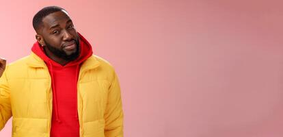 Doubtful displeased african american bearded male customer pointing up index finger squinting cringing disbelief hesitant uncertain product quality, standing questioned frustrated pink background photo
