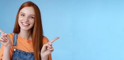 Friendly happy laughing pretty redhead girl female student showing lots opportunities advice make choice pointing sideways left right introducing different product grinning gladly, blue background photo