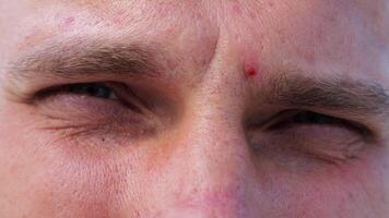 Close up to upset male face looking into camera with a disappointing sight. Upset facial expression of man with blue eyes. Unhappy gaze of despairing young guy. Slow motion video