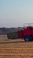 Harvesting dry grass. Agricultural works in the field. Tractor is pressing hay into square bale on the natural yellow field background. Vertical video