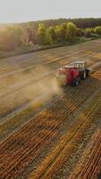 Red tractor on the yellow field in a sunny day. Harvesting dried grass in summer. Agricultural machine is baling hay into square bundles. Aerial view. Vertical video