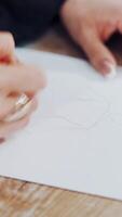 Female's hands drawing sketches of clothes on paper in her workplace. Clothes designer or tailor sketching with a pencil on a table. Vertical video