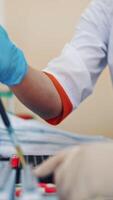 Professional laboratory technician fills vial with liquid and puts in the rack. Medical workers with test tubes of blood sample in the laboratory. Vertical video