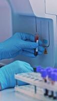 Close-up of female hands filling the tube with blood from the automated machine. Technician uses laboratory equipment while working with samples in tubes indoors. Vertical video