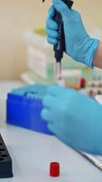 Laboratory worker is putting tubes with blood on a rack. Hands of a female nurse in sterile gloves working with vials on the table in a laboratory. Close-up. Vertical video