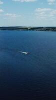 Panoramic view of a wide blue river among nature. Motor boat floating in the middle of the river in summer. Aerial view. Vertical video