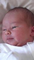 Sweet newborn boy is lying on the bed and turning his little head back and forth. Yawning tiny kid in a white costume. Close-up from above. Vertical video