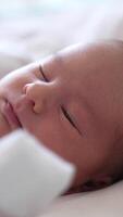 Tiny child is slowly blinking its eyes and gradually falling asleep. Sweet baby in white clothes on a white bed. Beautiful baby face close up. Vertical video