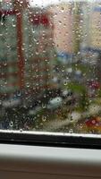 Glass window in rainy weather. Raindrops falling down on the urban background. View from the flat on the rainy weather in the city. Vertical video