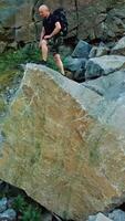 A man in a black t-shirt and a backpack comes to the edge of a large stone and raises his hands up. Tourist got to the center of stone quarry. Vertical video