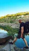 A tourist in summer clothes walks on the edge of a quarry with huge stones and looks at the beautiful lake and the nature around it. Beautiful view. Vertical video