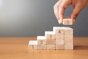 Women hand putting a wooden block on top and arranging wooden blocks stacking on wooden table. photo