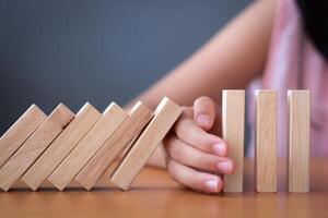 Girl's hand Stopping Falling wooden Dominoes effect from continuous toppled or risk. photo