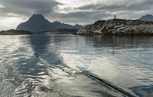 Norwegian seascape, lighthouse on the island, rocky coast with dramatic skies, the sun breaks through the clouds, sheer cliffs, small islands illuminated by the sun photo