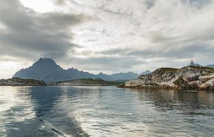 Norwegian seascape, lighthouse on the island, rocky coast with dramatic skies, the sun breaks through the clouds, sheer cliffs, small islands illuminated by the sun photo