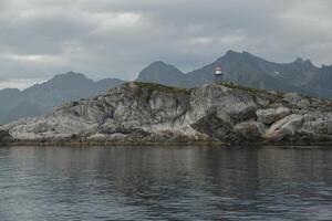 Norwegian seascape, lighthouse on the island, rocky coast with dramatic skies, the sun breaks through the clouds, sheer cliffs, small islands illuminated by the sun photo
