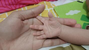 A mother's hand gently holds the tiny hand of her newborn baby. The image evokes a sense of love, care, and the bond between parent and child. photo